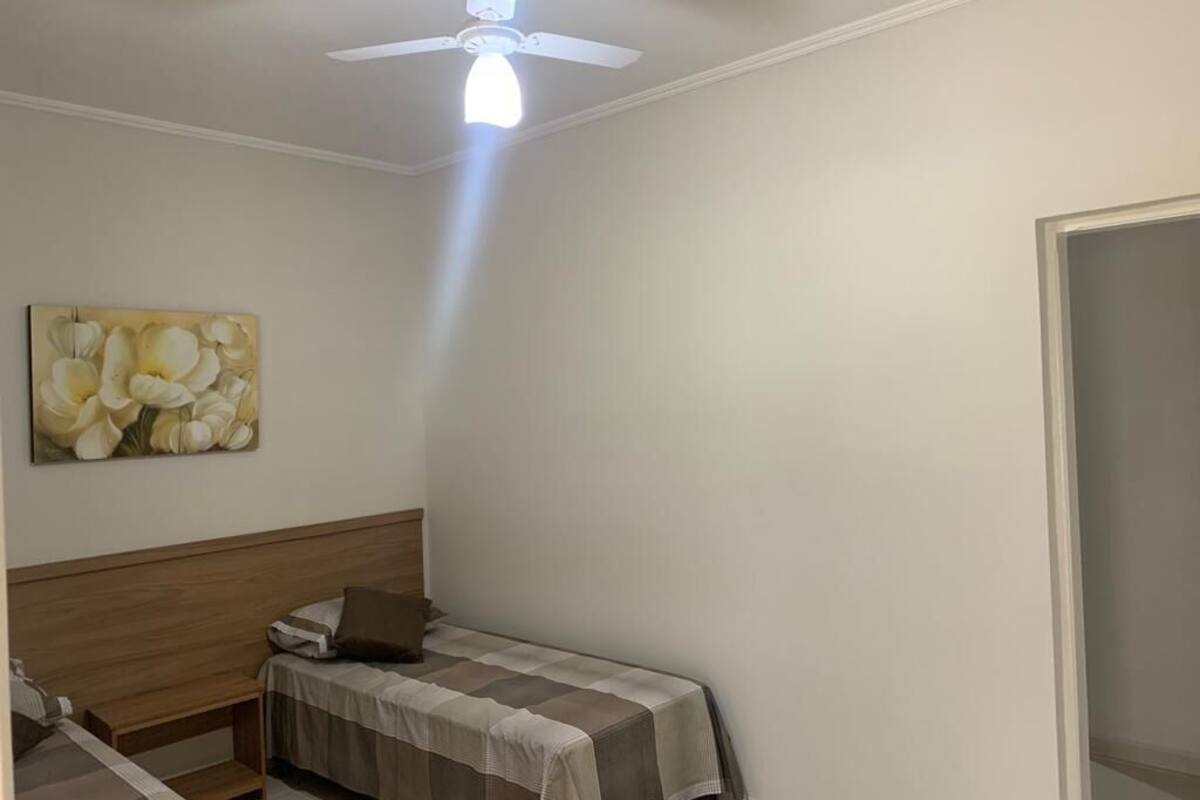 Ein Schlafzimmer mit einem Einzelbett, einem Deckenventilator und einem Gemälde an der Wand.