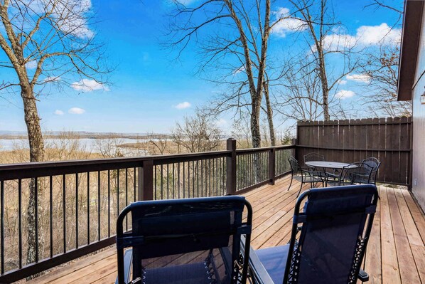 A wooden deck with two chairs and a table, overlooking a snowy landscape and trees. - Skipjack Cottage Branson (Branson West)