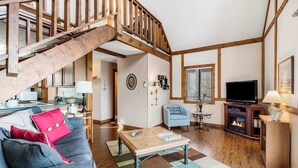 A cozy living room with a wooden staircase, a television, a fireplace, and a chessboard on a coffee table. - Skipjack Cottage Branson (Branson West)