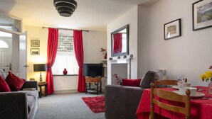 Ein gemütliches Wohnzimmer mit Kamin, Fernseher und Essbereich mit Tisch für zwei Personen.