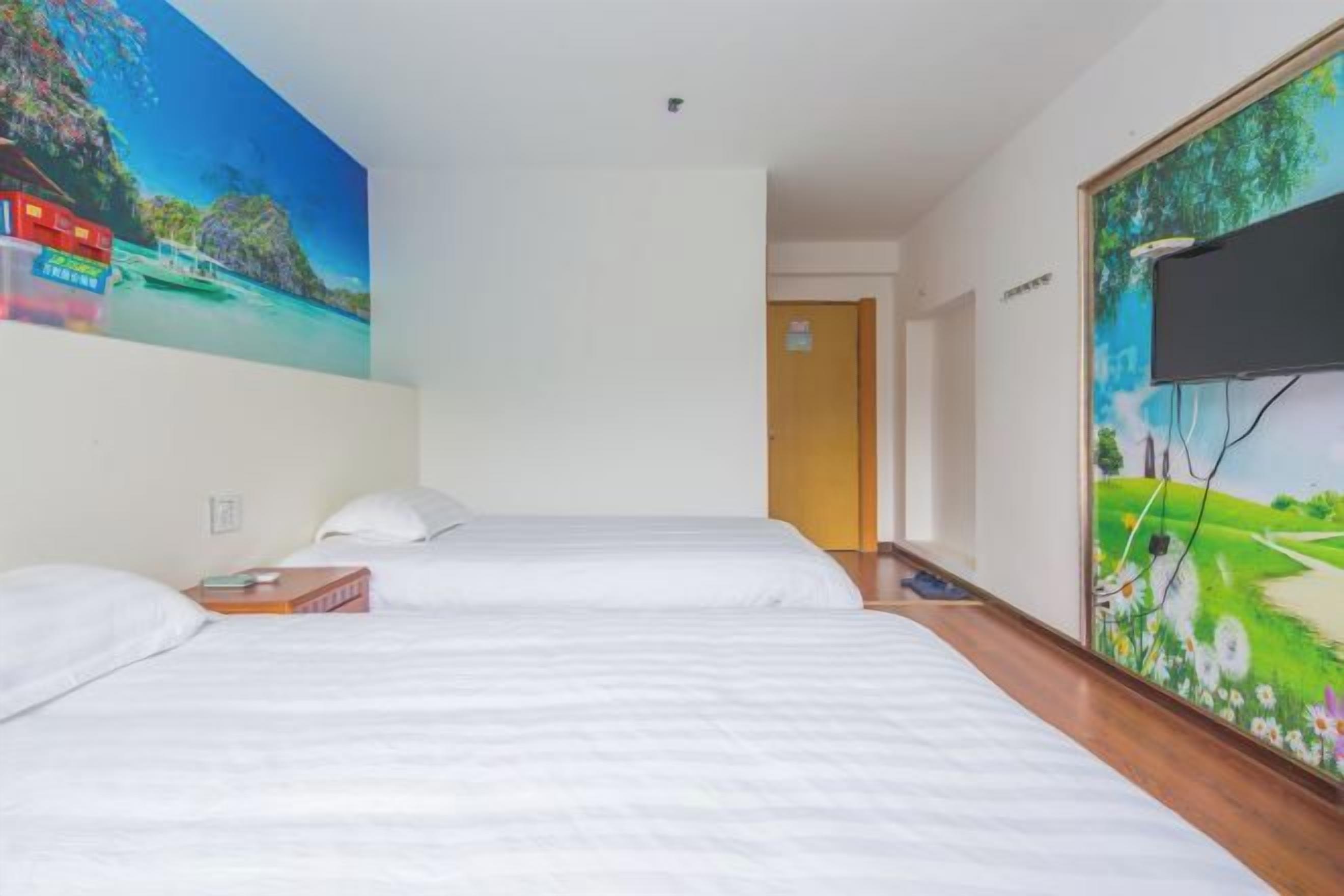 Une chambre d’hôtel avec deux lits, un tableau représentant une plage tropicale et un téléviseur fixé au mur.