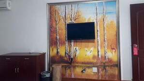 A room with a mounted TV, a wooden cabinet, a trash bin, and a painting of a forest scene. - Yandang Mountain Xiufeng Tower (Yueqing)