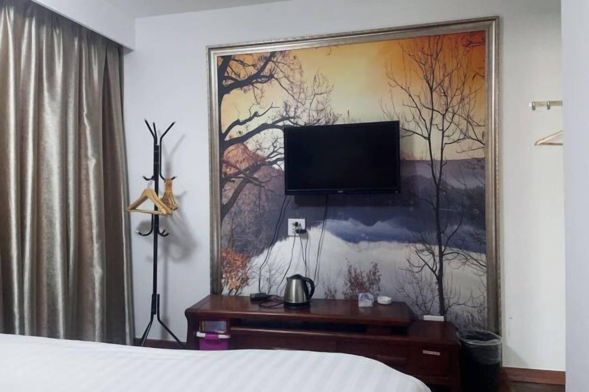 Ein Hotelzimmer mit einem Bett, einem wandmontierten Flachbildfernseher, einem Holzschrank, einem Kleiderständer und einem Landschaftsbild.