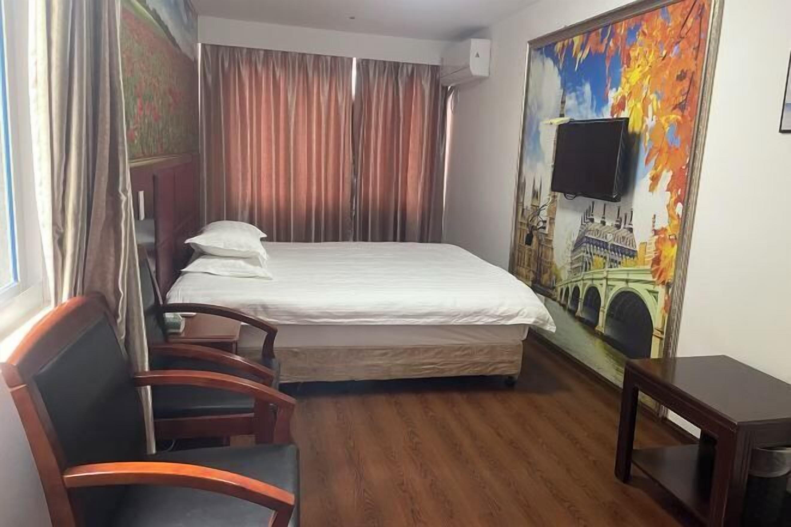 Quarto de hotel com cama, cadeira, mesa pequena, TV fixada na parede e pintura de uma ponte.