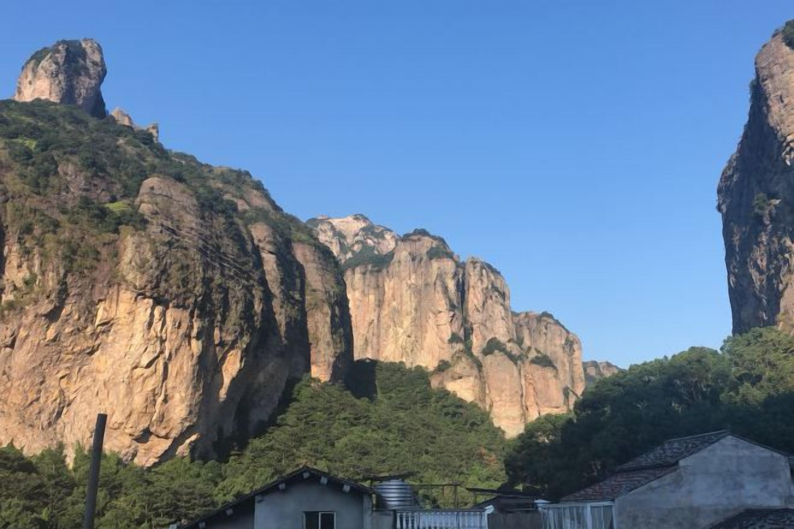 A mountain landscape with a prominent rock formation and a small building in the foreground.