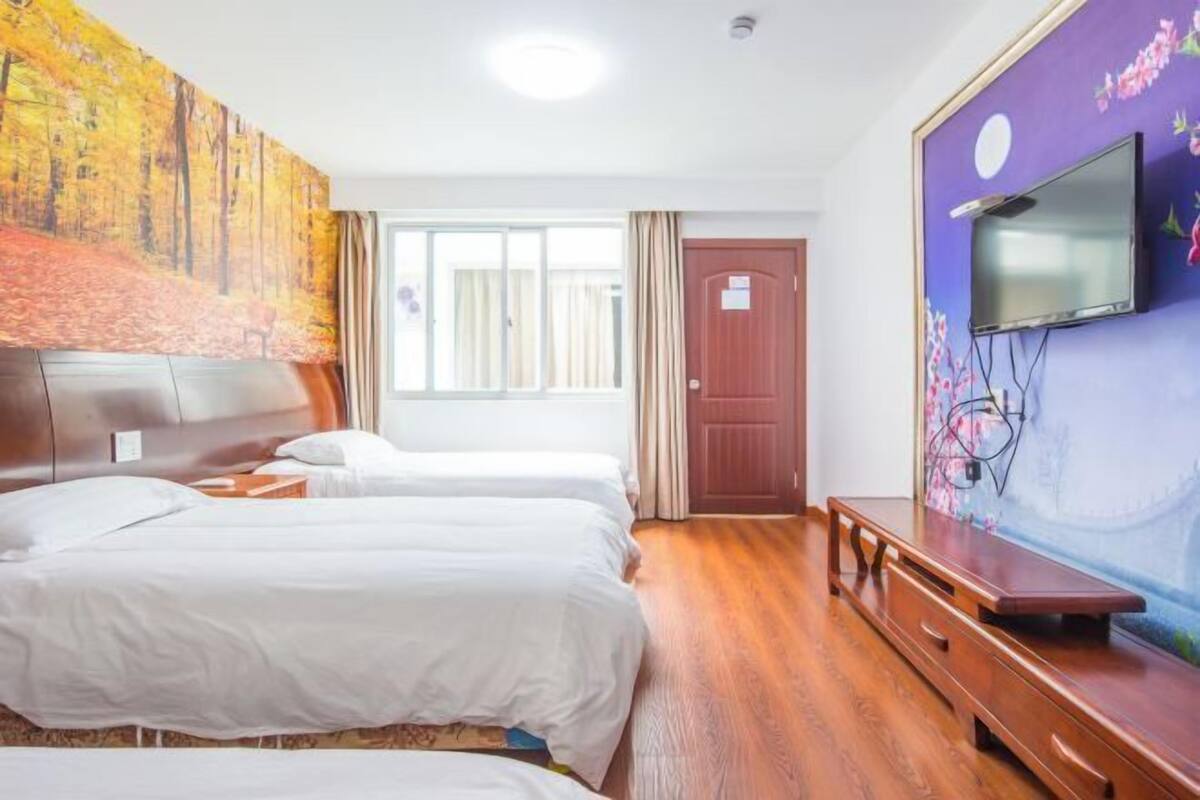 Ein Hotelzimmer mit zwei Betten, einem Fernseher, einer hölzernen Bank und einem großen Fenster.