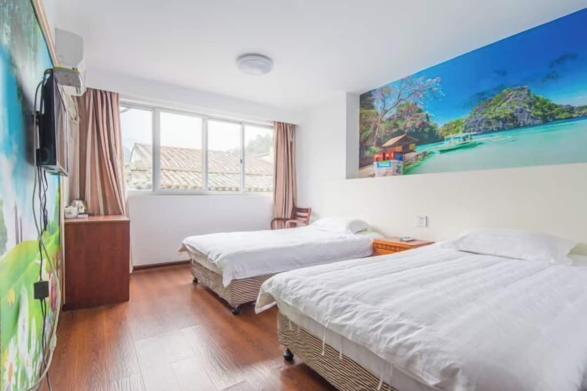 Ein Hotelzimmer mit zwei Betten, einem Fenster mit Vorhängen, einem Bild an der Wand und Holzboden.
