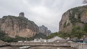 A rooftop terrace with a view of rocky cliffs and a small building in the background. - Yandang Mountain Xiufeng Tower (Yueqing)