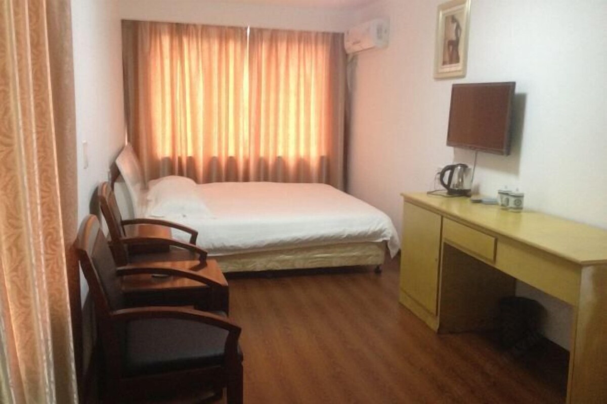A hotel room with a bed, a desk, a chair, a television, and a window with curtains.