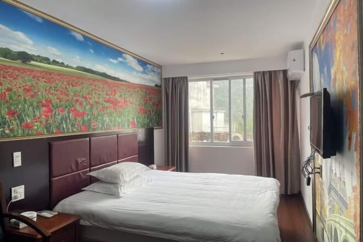 Ein Hotelzimmer mit einem großen Bett, einem Nachttisch, einem Fernseher und einem Fenster mit Vorhängen.