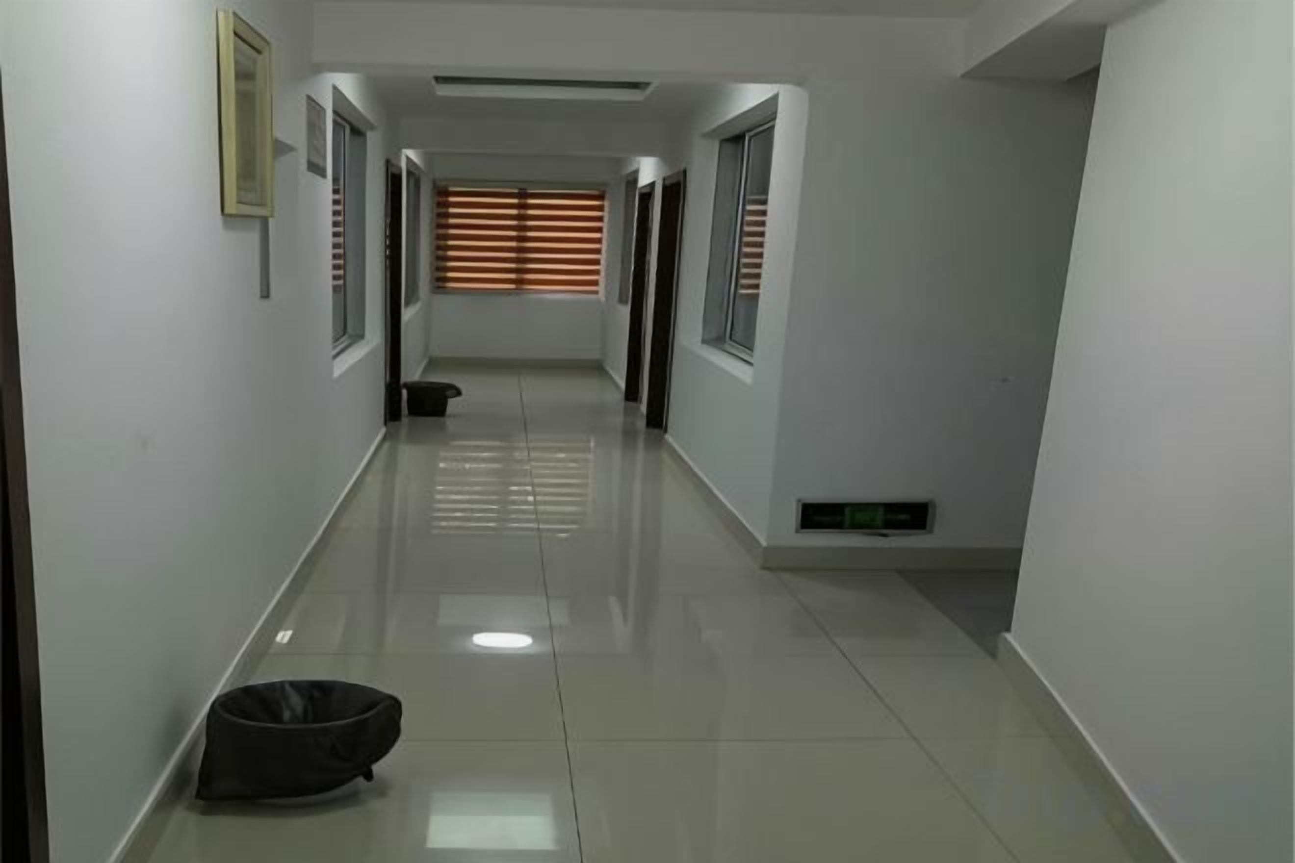A hallway with a shiny floor, doors on both sides, and a window with blinds at the end.