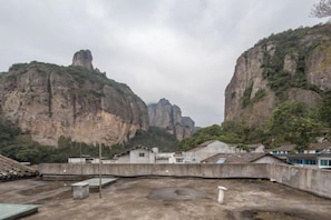 Un pati amb sòl de formigó, alguns edificis i una gran formació rocosa al fons.