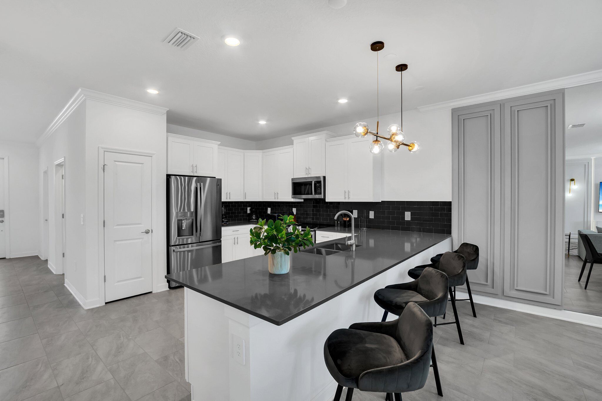 Une cuisine moderne avec des meubles blancs, un îlot central doté de tabourets, des appareils en acier inoxydable et un luminaire suspendu.