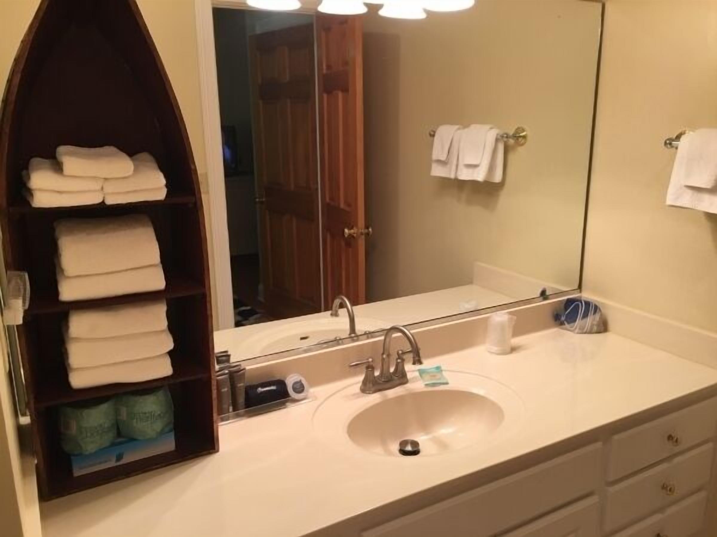 Une salle de bain avec un lavabo, un miroir et des étagères où sont pliées des serviettes.