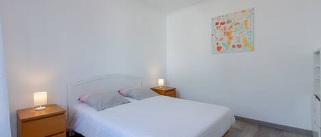 A bedroom with a bed, two bedside tables, a nightstand, a wall art piece, and a white wardrobe.