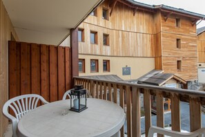 En træterrasse med et rundt bord og stole, en lygte samt udsigt til omkringliggende bygninger.