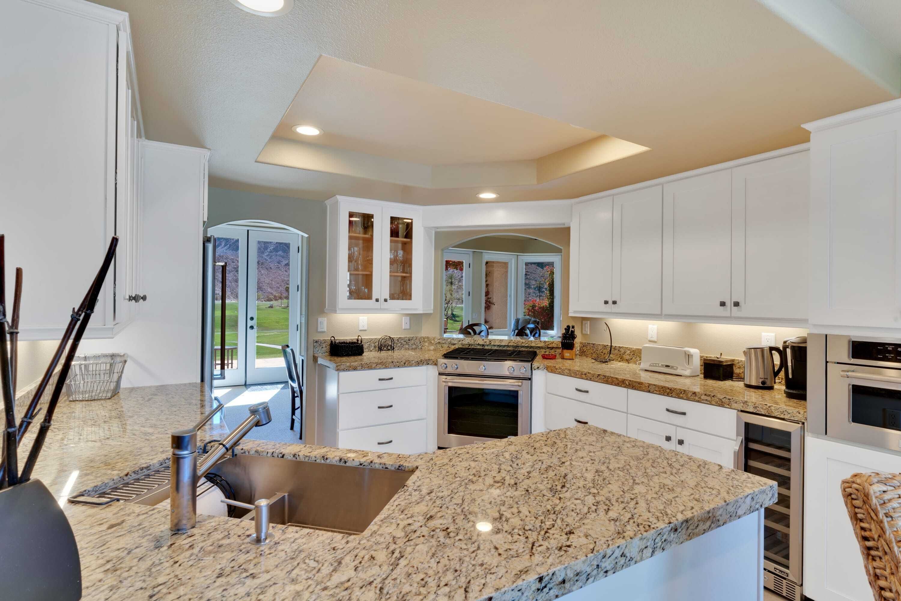Una cocina moderna con gabinetes blancos, encimeras de granito, electrodomésticos de acero inoxidable y una isla grande con un fregadero.