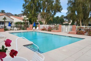 A rectangular pool with a white fence and chairs around it.