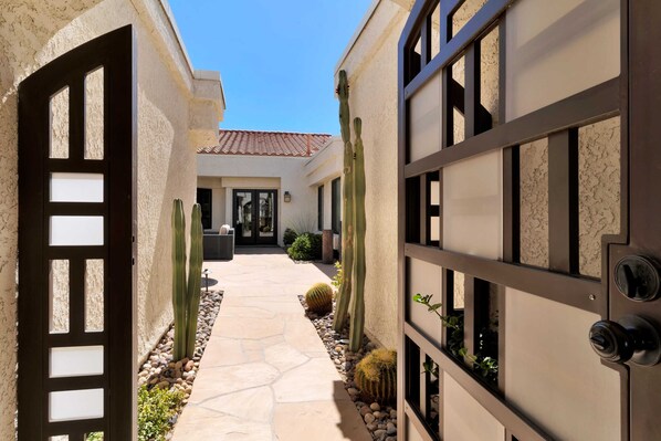 A courtyard with a stone pathway, cacti, and a building with a tiled roof.