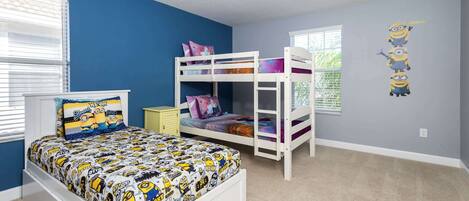 A child's bedroom with a bunk bed, a single bed, and a window with blinds.