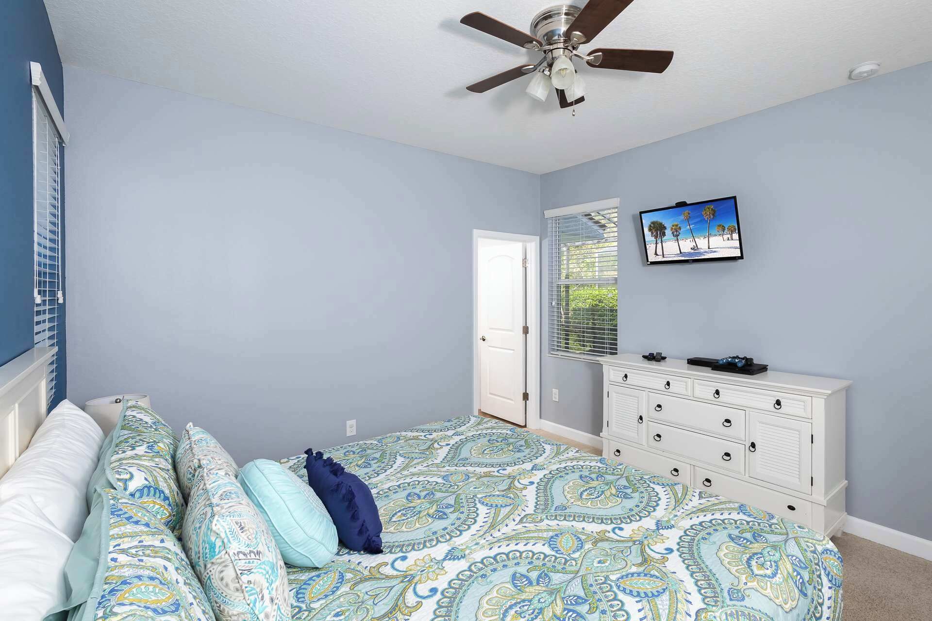 Ein Schlafzimmer mit Bett, Schminktisch, Deckenventilator und Fernseher an der Wand.