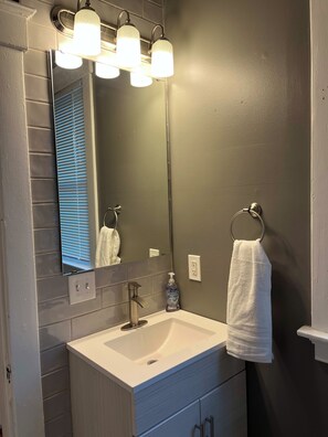 A bathroom with a white sink, a mirror, and three wall-mounted lights. - Rolston 1, One Bedroom Unit near Xavier, Downtown (Cincinnati)
