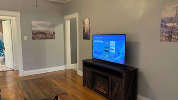 Una sala de estar con un televisor de pantalla plana sobre un soporte de madera, una chimenea y una puerta que da a otra habitación.