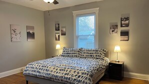 A bedroom with a bed, two bedside lamps, a ceiling fan, and a window with blinds.
