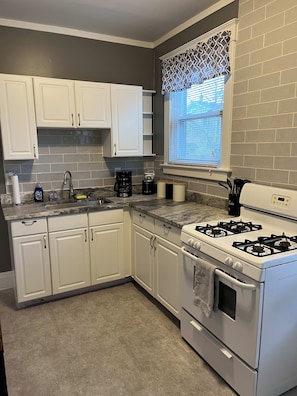 A kitchen with white cabinets, a gas stove, a coffee maker, and a window with patterned curtains.