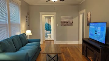 A living room with a sofa, a coffee table, a fireplace, and a television displaying a streaming service interface.