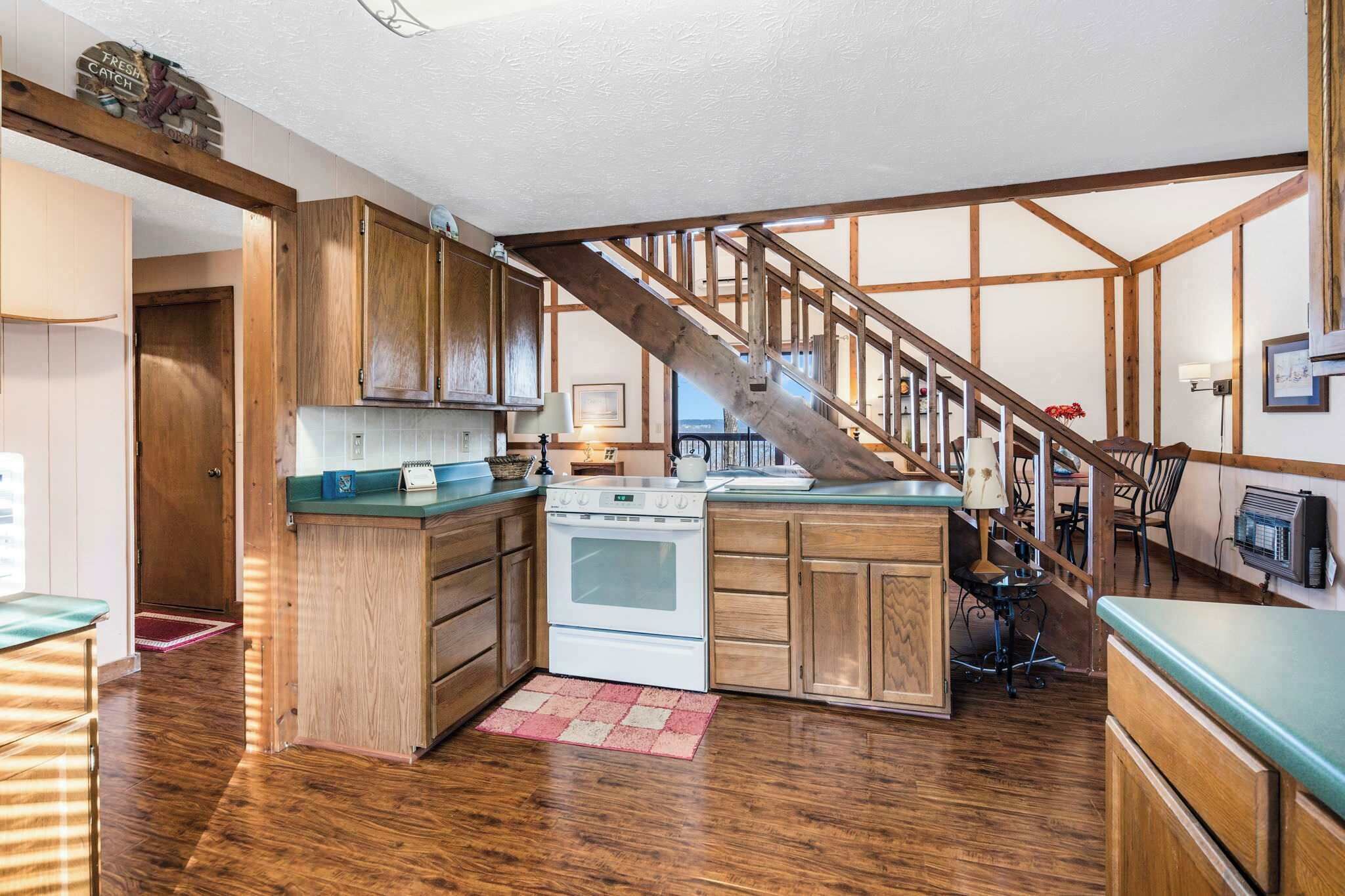 Une cuisine avec des meubles de rangement en bois, une cuisinière et un escalier.