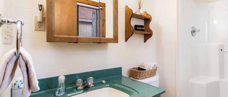 A bathroom with a green countertop sink, a wooden-framed mirror, a shower, and a white toilet.