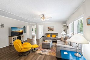 A living room with a sofa, ottoman, and yellow chair, a television, and a ceiling fan. - 🏝️Close to Beach-Pet Friendly-Private Home-3BR Beachin' Fun (Navarre)