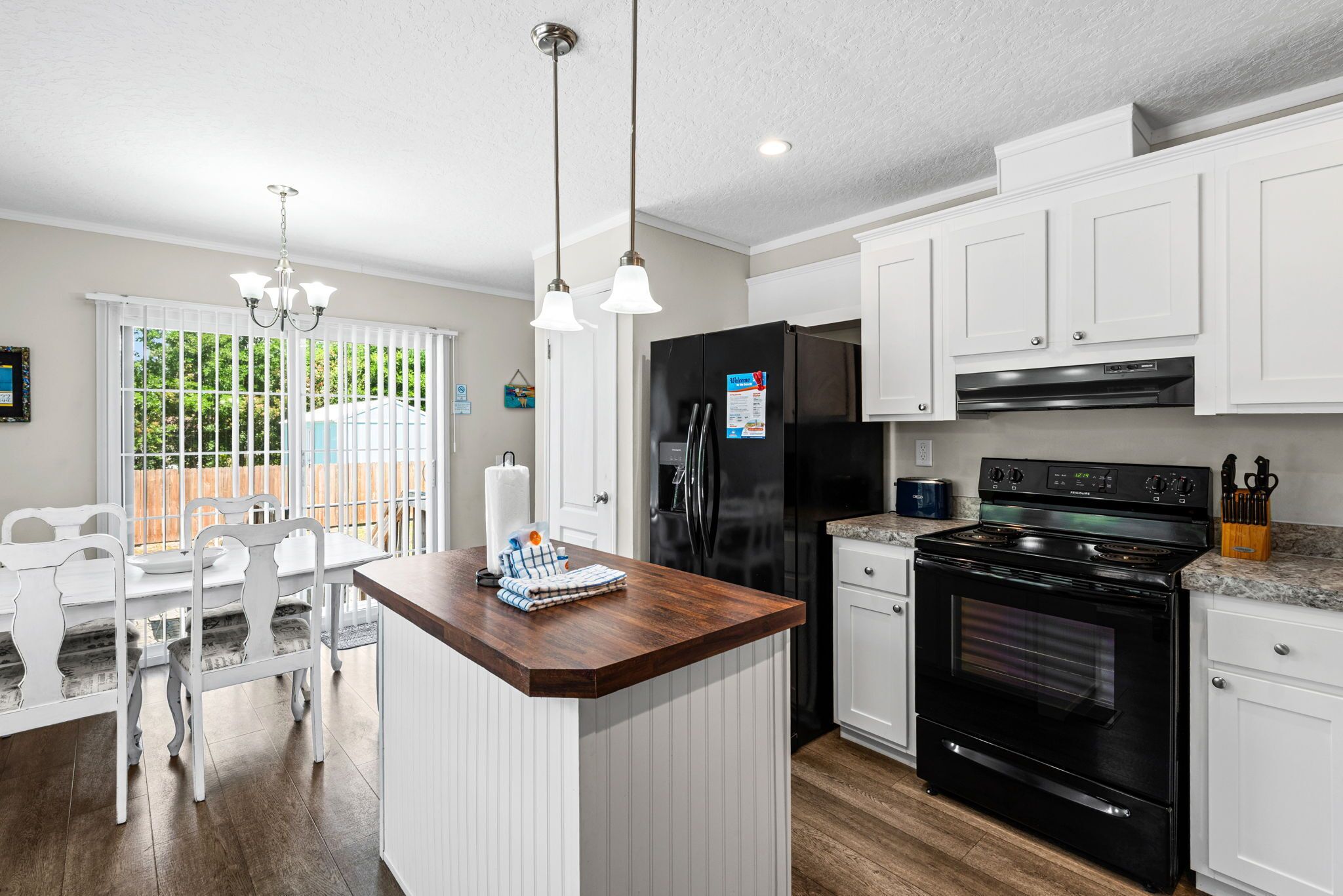 A modern kitchen with white cabinets, a black refrigerator, a stove, and a dining area with a white table and chairs.