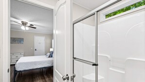 Ein Schlafzimmer mit Bett, Deckenventilator, weißer Tür und Duschbereich.