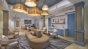 Een ruime lobby met een grote zithoek, een receptiebalie en een moderne kroonluchter.