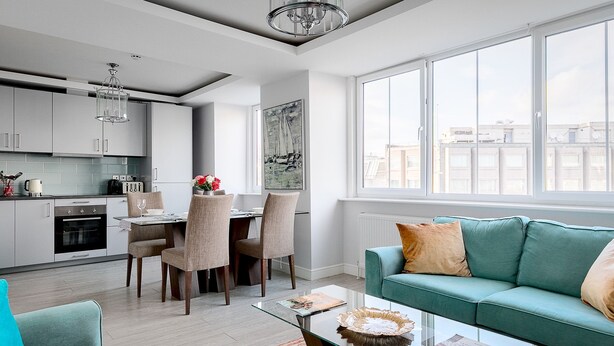 A modern kitchen with white cabinets, a dining area with chairs, a teal sofa, and a glass coffee table. - Penthouse apartment on Cromwell road (London)
