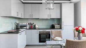A modern kitchen with grey cabinets, a black countertop, a stainless steel oven, and a dining area with a table set for two. - Penthouse apartment on Cromwell road (London)