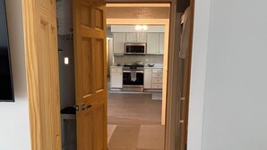 Un couloir menant à une cuisine avec des portes en bois, un four à micro-ondes et un sol carrelé.