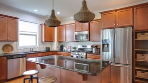 A modern kitchen with wooden cabinets, stainless steel appliances, a granite countertop, and pendant lighting.