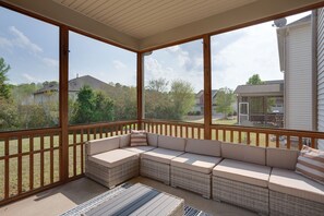 Un espacio al aire libre techado con un banco acolchado y una mesa pequeña, con vista a un barrio residencial.