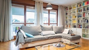 Un salon moderne avec un canapé gris, une table basse en verre et une bibliothèque remplie de livres.