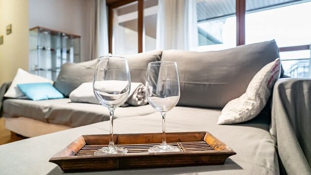 Un salon moderne avec un canapé, deux verres sur un plateau et une fenêtre avec des rideaux.