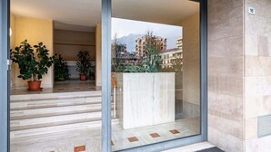 Une entrée d’immeuble moderne avec une porte en verre, un escalier en marbre et des plantes en pot.