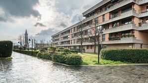 Un immeuble résidentiel à plusieurs étages, doté de balcons, d’une allée pavée et d’un beffroi en arrière-plan.