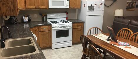 A kitchen with wooden cabinets, a gas stove, a microwave, a refrigerator, a sink, and a dining table with chairs.