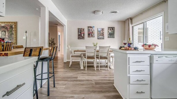 A modern kitchen with white cabinetry, a dining area with a table and chairs, and a large window providing natural light. - Taste of Tuscany - Hot Tub, Fire Pit & Pool Table (Fredericksburg)