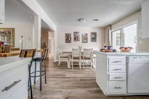 Una cocina moderna con armarios blancos, un comedor con mesa y sillas blancas, y un ventanal que proporciona luz natural.