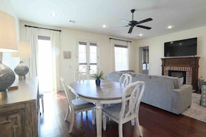 A dining area with a round table, white chairs, and a chandelier. There is a sofa and a television in the background. - The Sadie, Walk to Campus, by Velvet Ditch Villas (Oxford)