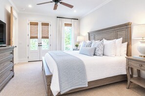 Une chambre à coucher comprenant un lit, une table de chevet, une commode, un ventilateur de plafond et une fenêtre avec des rideaux.